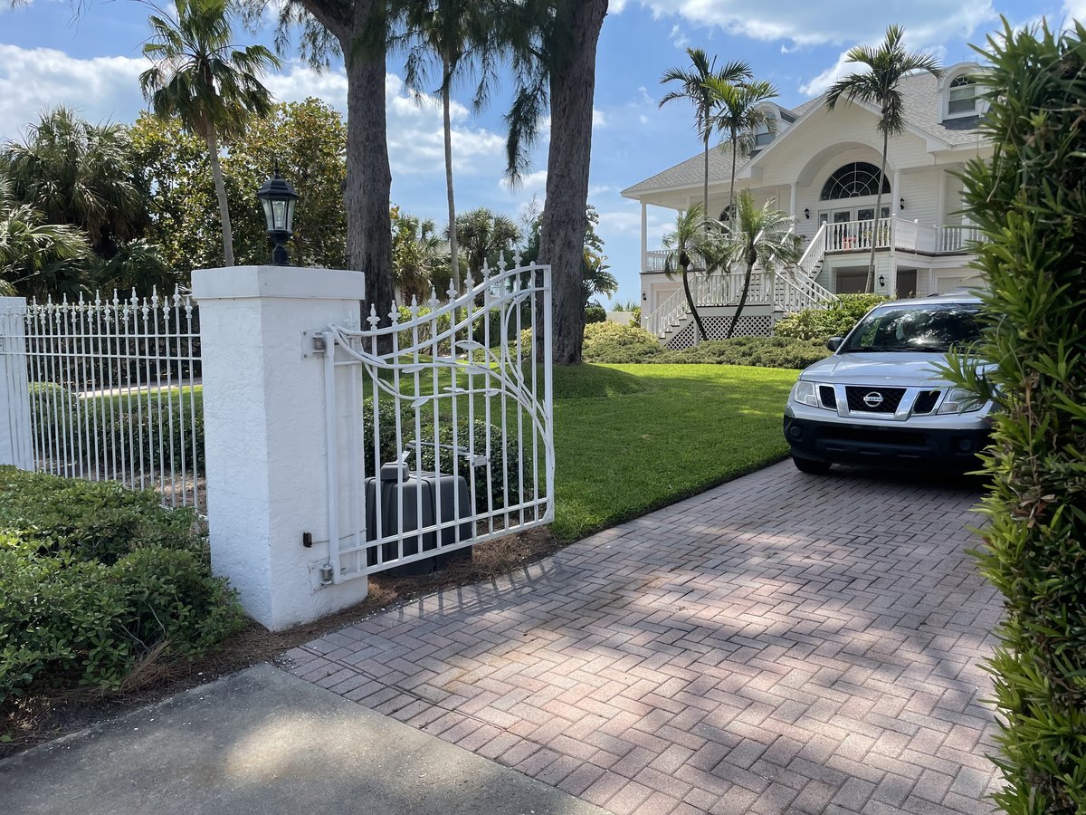 Palm-lined garden entrance with a white gate and driveway
